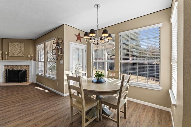 dining space featuring baseboards, wood finished floors, a healthy amount of sunlight, and a fireplace with raised hearth