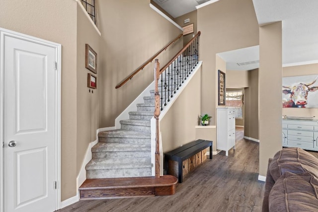 staircase with baseboards, wood finished floors, a towering ceiling, and crown molding