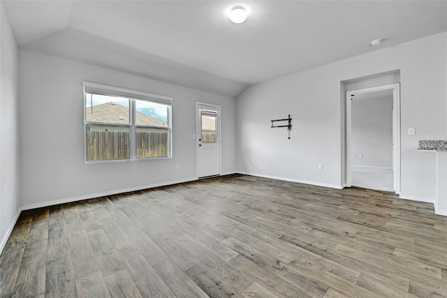 unfurnished room featuring baseboards, lofted ceiling, and wood finished floors