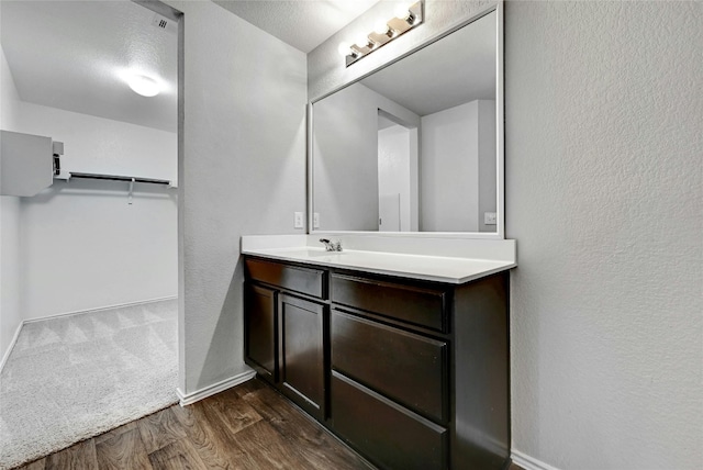 bathroom with a textured wall, vanity, baseboards, and wood finished floors