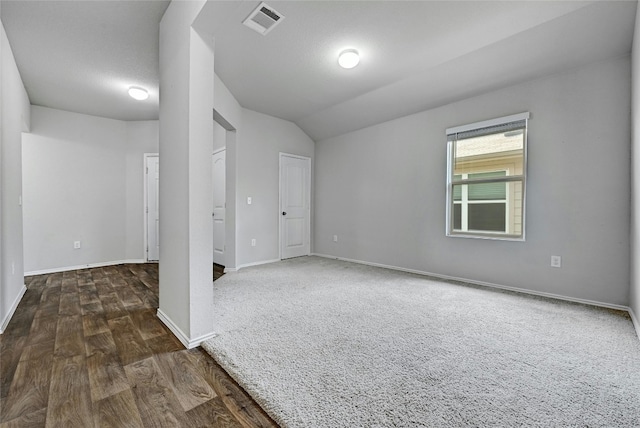 empty room featuring vaulted ceiling, dark wood-style floors, visible vents, and baseboards