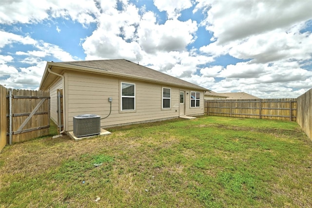 rear view of property featuring central air condition unit, a lawn, and a fenced backyard