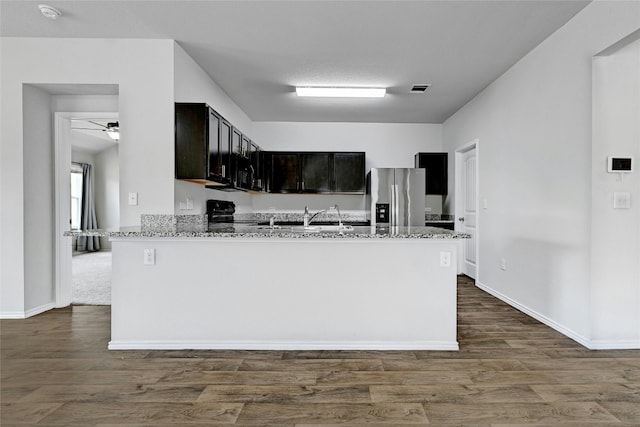 kitchen featuring dark wood-style flooring, stainless steel fridge, a sink, and light stone countertops