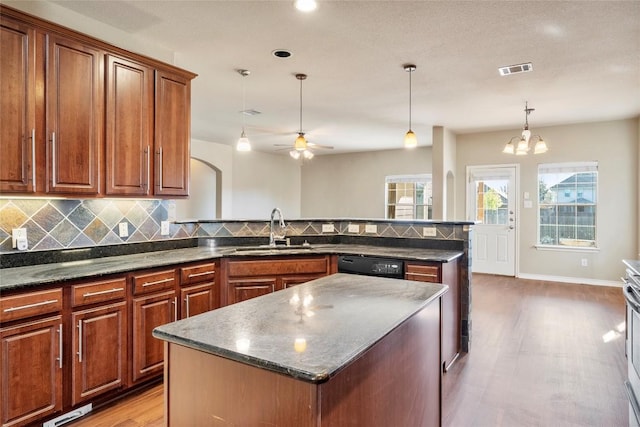 kitchen featuring visible vents, light wood finished floors, a peninsula, a sink, and decorative backsplash