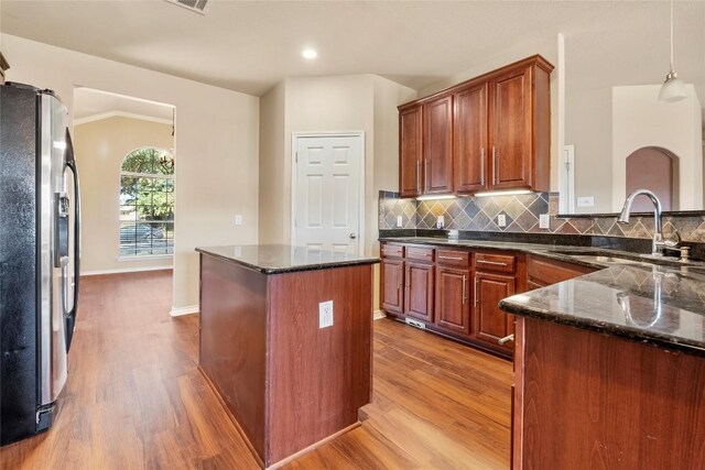 kitchen featuring a sink, a kitchen island, tasteful backsplash, wood finished floors, and stainless steel fridge with ice dispenser