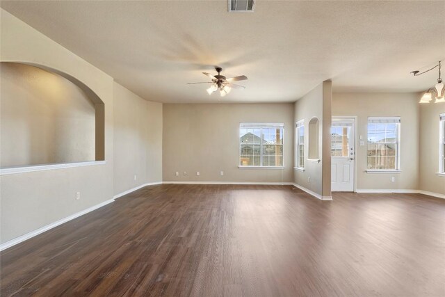 empty room with visible vents, ceiling fan with notable chandelier, dark wood-type flooring, and baseboards