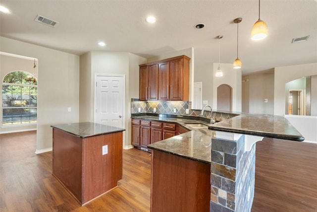 kitchen featuring visible vents, a kitchen island, arched walkways, a sink, and tasteful backsplash