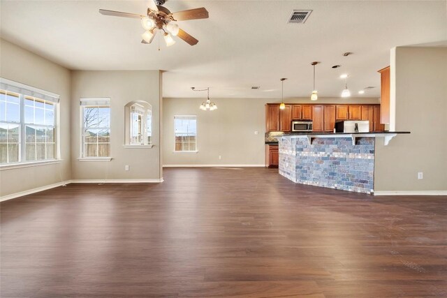 unfurnished living room with a wealth of natural light, visible vents, baseboards, and dark wood finished floors