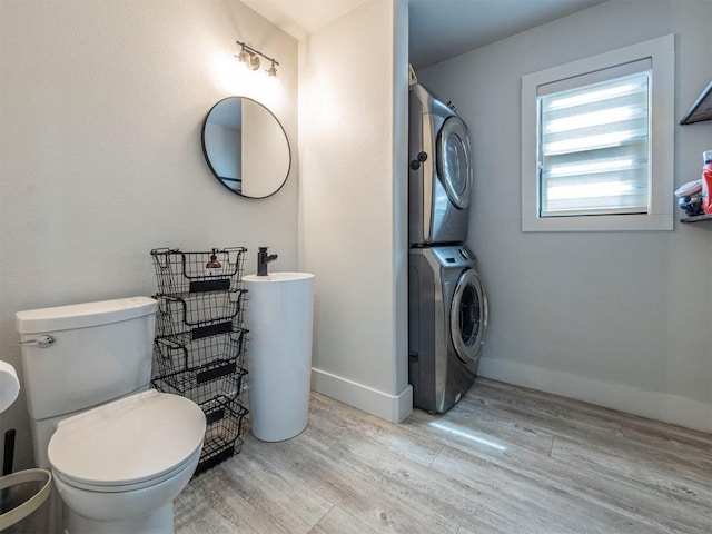 bathroom featuring estacked washer and dryer, wood finished floors, baseboards, and toilet