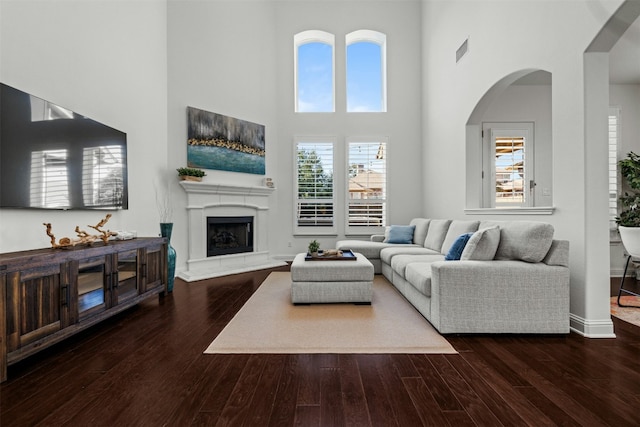 living area with visible vents, a fireplace with raised hearth, wood finished floors, and a towering ceiling