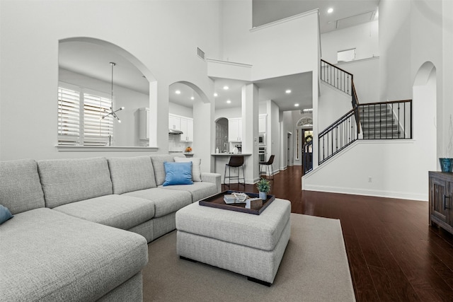 living area with visible vents, dark wood finished floors, baseboards, a towering ceiling, and stairs