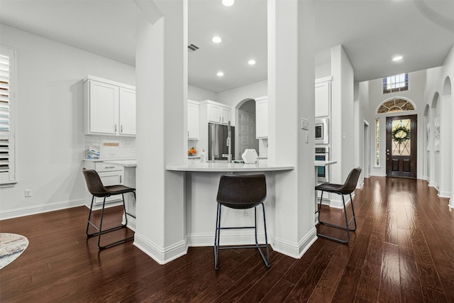 kitchen featuring a kitchen breakfast bar, stainless steel appliances, arched walkways, decorative backsplash, and dark wood-style flooring