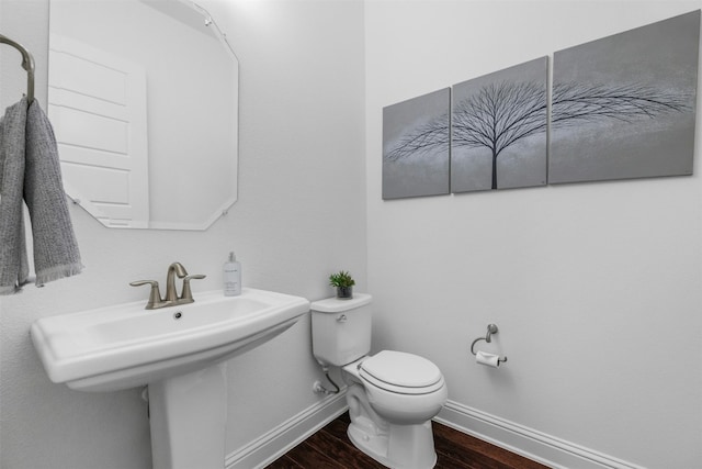 half bathroom featuring a sink, baseboards, toilet, and wood finished floors