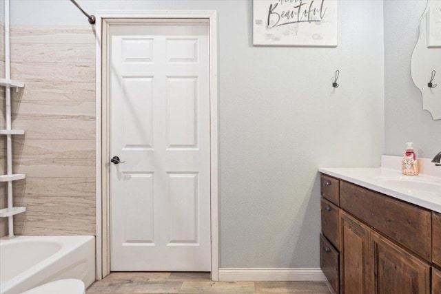 bathroom with bathtub / shower combination, vanity, baseboards, and wood finished floors