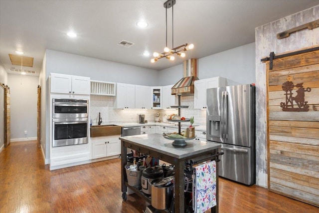 kitchen with stainless steel appliances, a barn door, tasteful backsplash, and white cabinetry