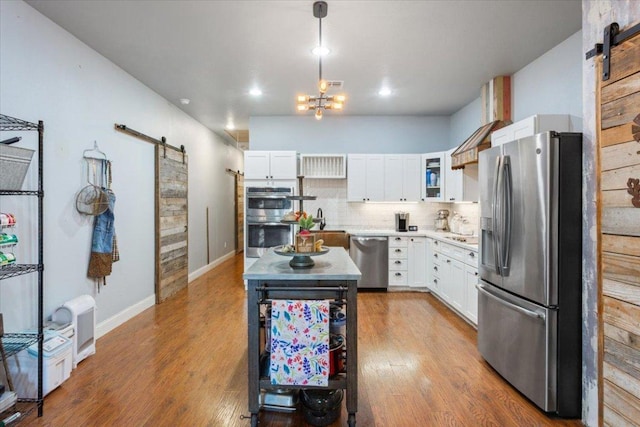 kitchen featuring decorative backsplash, white cabinets, stainless steel appliances, and a barn door