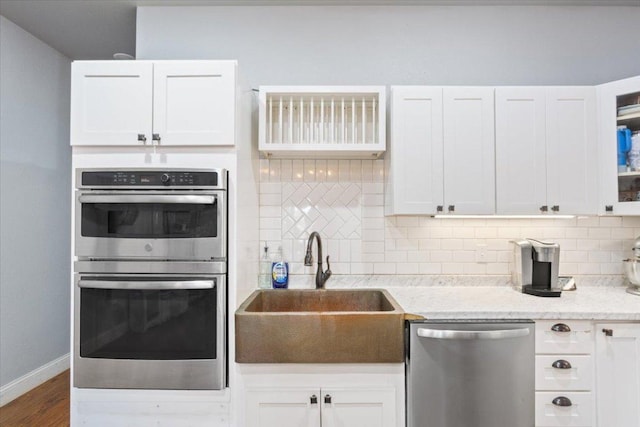 kitchen with decorative backsplash, white cabinets, appliances with stainless steel finishes, and a sink