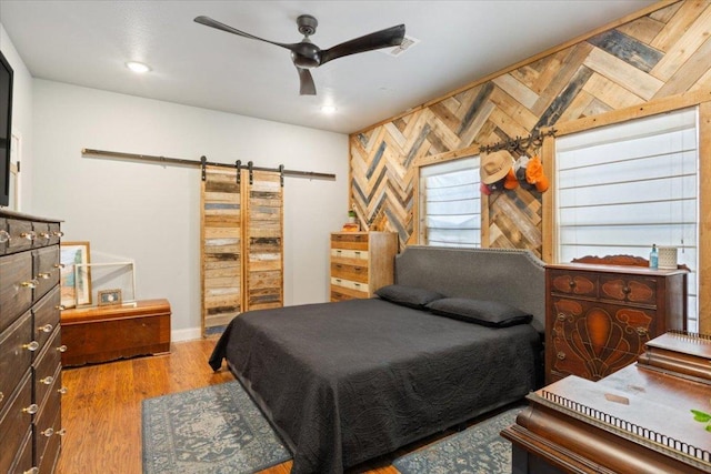 bedroom with wood finished floors, recessed lighting, a barn door, wood walls, and ceiling fan