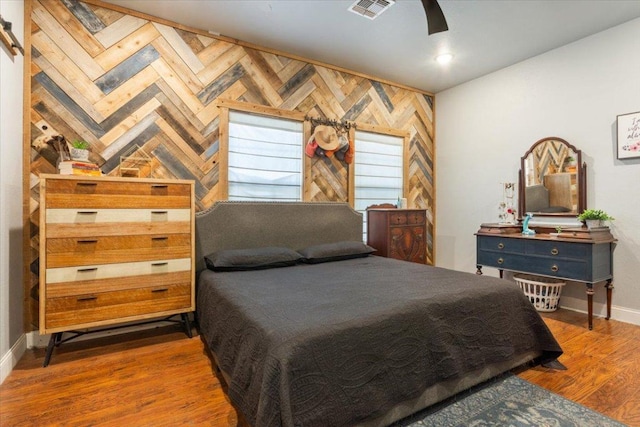 bedroom featuring a ceiling fan, wood finished floors, visible vents, baseboards, and wood walls