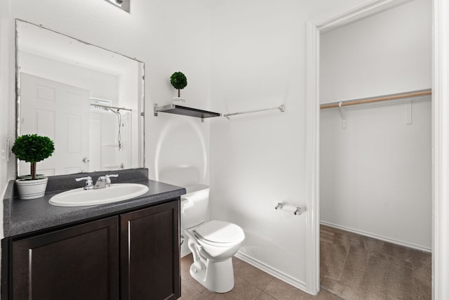 bathroom with tile patterned floors, a walk in closet, toilet, and vanity