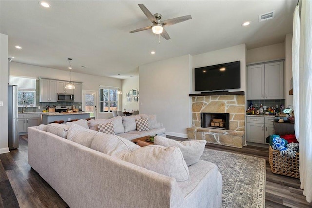 living room with visible vents, dark wood-style floors, recessed lighting, a stone fireplace, and baseboards