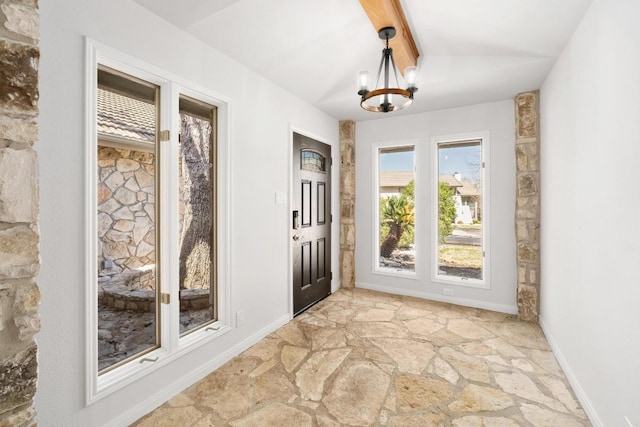 foyer entrance with a notable chandelier, stone floors, lofted ceiling with beams, and baseboards