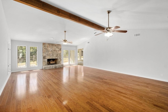 unfurnished living room featuring visible vents, a ceiling fan, wood finished floors, a stone fireplace, and vaulted ceiling with beams