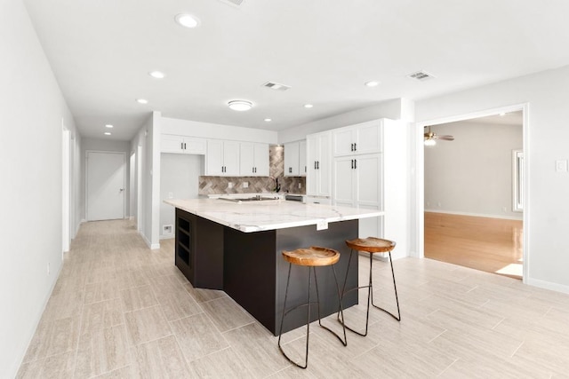 kitchen with light stone counters, visible vents, white cabinetry, and decorative backsplash