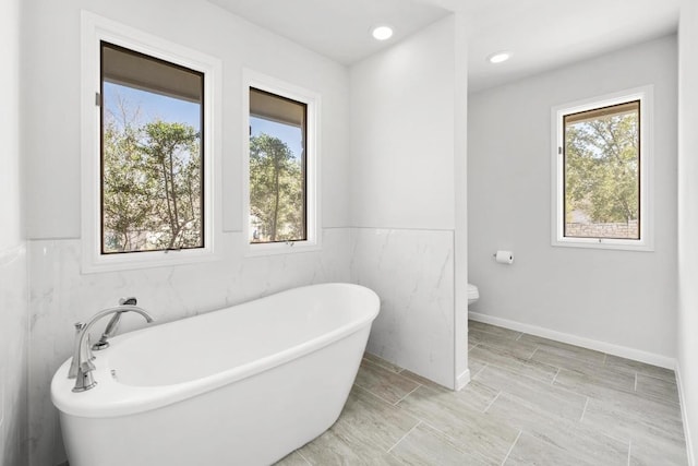 bathroom featuring recessed lighting, toilet, baseboards, and a freestanding tub