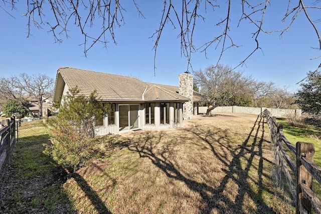 rear view of house with a chimney, a lawn, a tile roof, and a fenced backyard