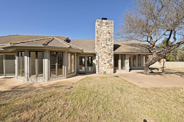 rear view of house with a chimney, a lawn, french doors, and a tile roof