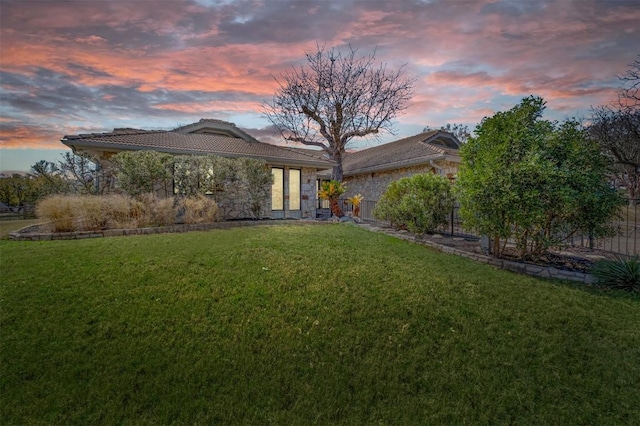 exterior space featuring stone siding, a tiled roof, a yard, and fence