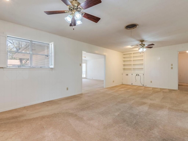 unfurnished room featuring visible vents, built in shelves, light colored carpet, and ceiling fan