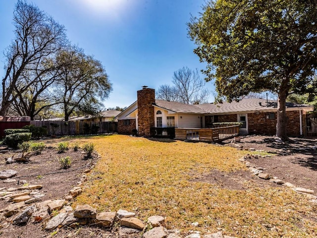 rear view of property with a deck, fence, a lawn, and a chimney