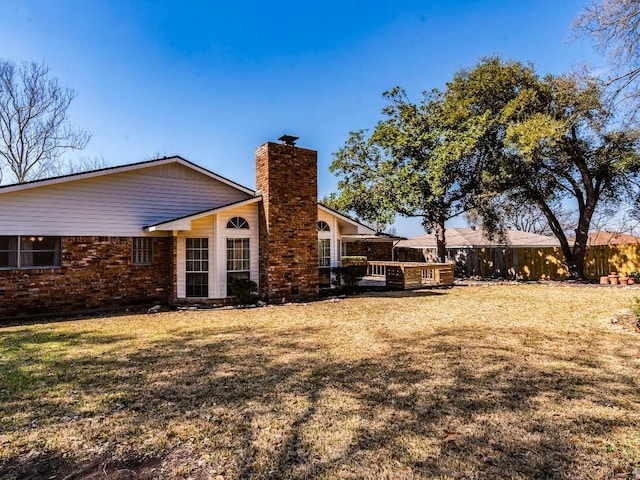 rear view of house with a yard, fence, brick siding, and a chimney