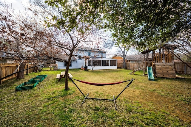 view of yard with a playground, a fenced backyard, and a sunroom