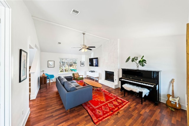 living area with wood finished floors, visible vents, a ceiling fan, lofted ceiling, and a stone fireplace