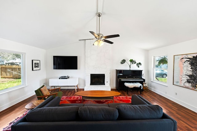 living area featuring a stone fireplace, a healthy amount of sunlight, lofted ceiling, and dark wood-style flooring