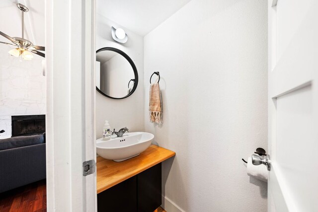 bathroom with a large fireplace, a ceiling fan, wood finished floors, and vanity