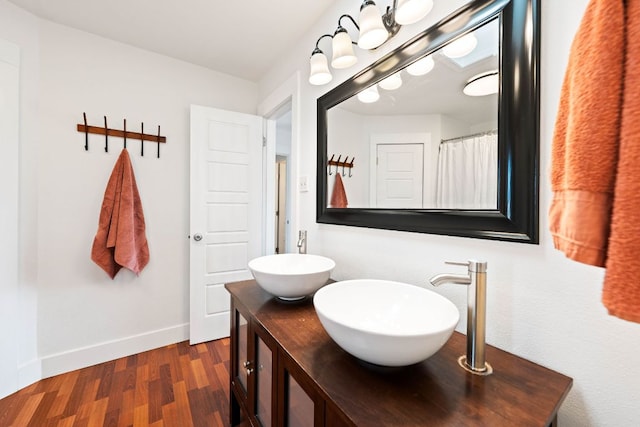 bathroom with double vanity, wood finished floors, baseboards, and a sink