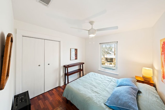 bedroom with a ceiling fan, dark wood-style floors, visible vents, and a closet