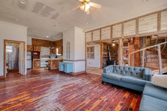 unfurnished living room with crown molding, a wood stove, a ceiling fan, and dark wood-style flooring