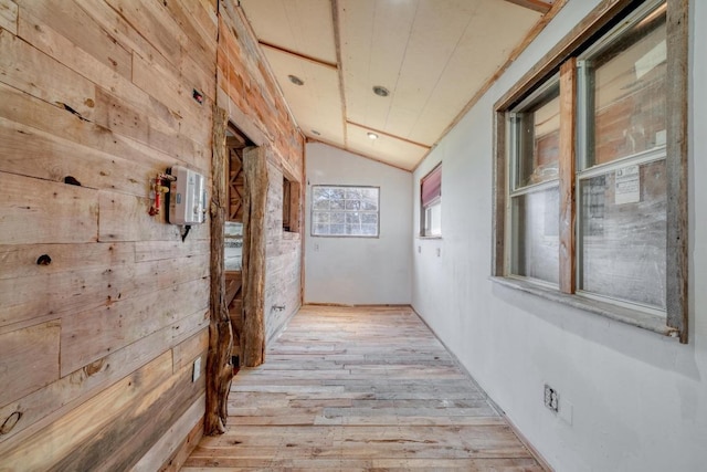 hallway with hardwood / wood-style flooring, wooden walls, and lofted ceiling