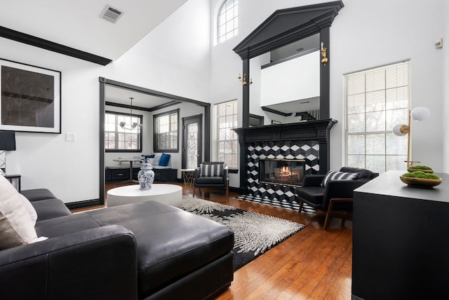 living area with visible vents, wood finished floors, crown molding, a towering ceiling, and a tile fireplace