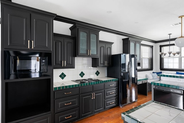 kitchen with tile countertops, wood finished floors, visible vents, ornamental molding, and black appliances