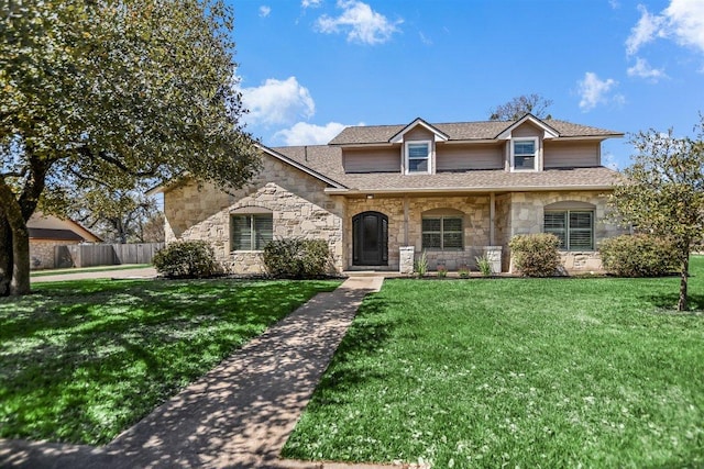 view of front of property featuring a front yard, fence, stone siding, and a shingled roof