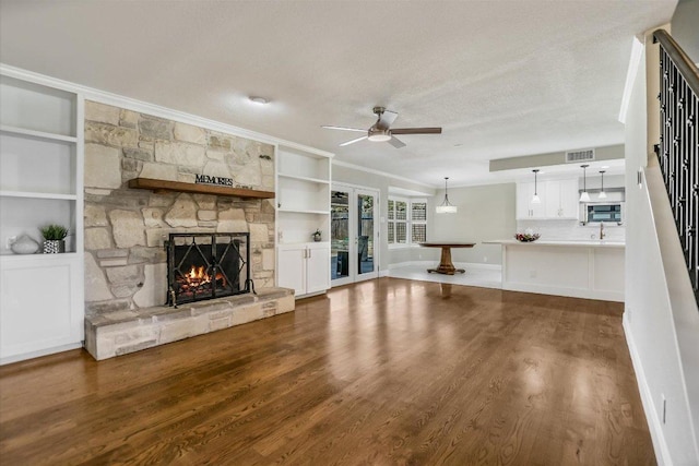 11402 Pencewood Dr, Austin, TX 78750 - unfurnished living room with ceiling fan, crown molding, a stone fireplace, wood finished floors, and a textured ceiling