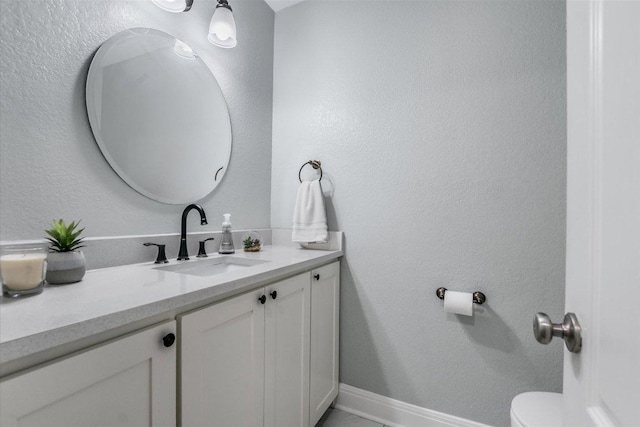 bathroom with toilet, vanity, baseboards, and a textured wall