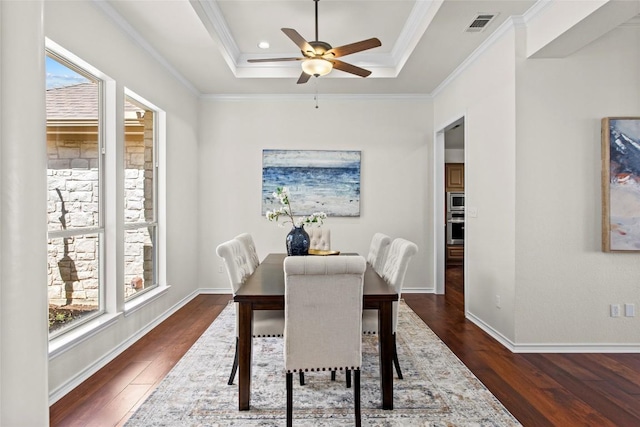 dining room with a wealth of natural light, visible vents, dark wood finished floors, and a tray ceiling