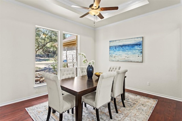 dining room featuring a raised ceiling, wood finished floors, baseboards, and ornamental molding